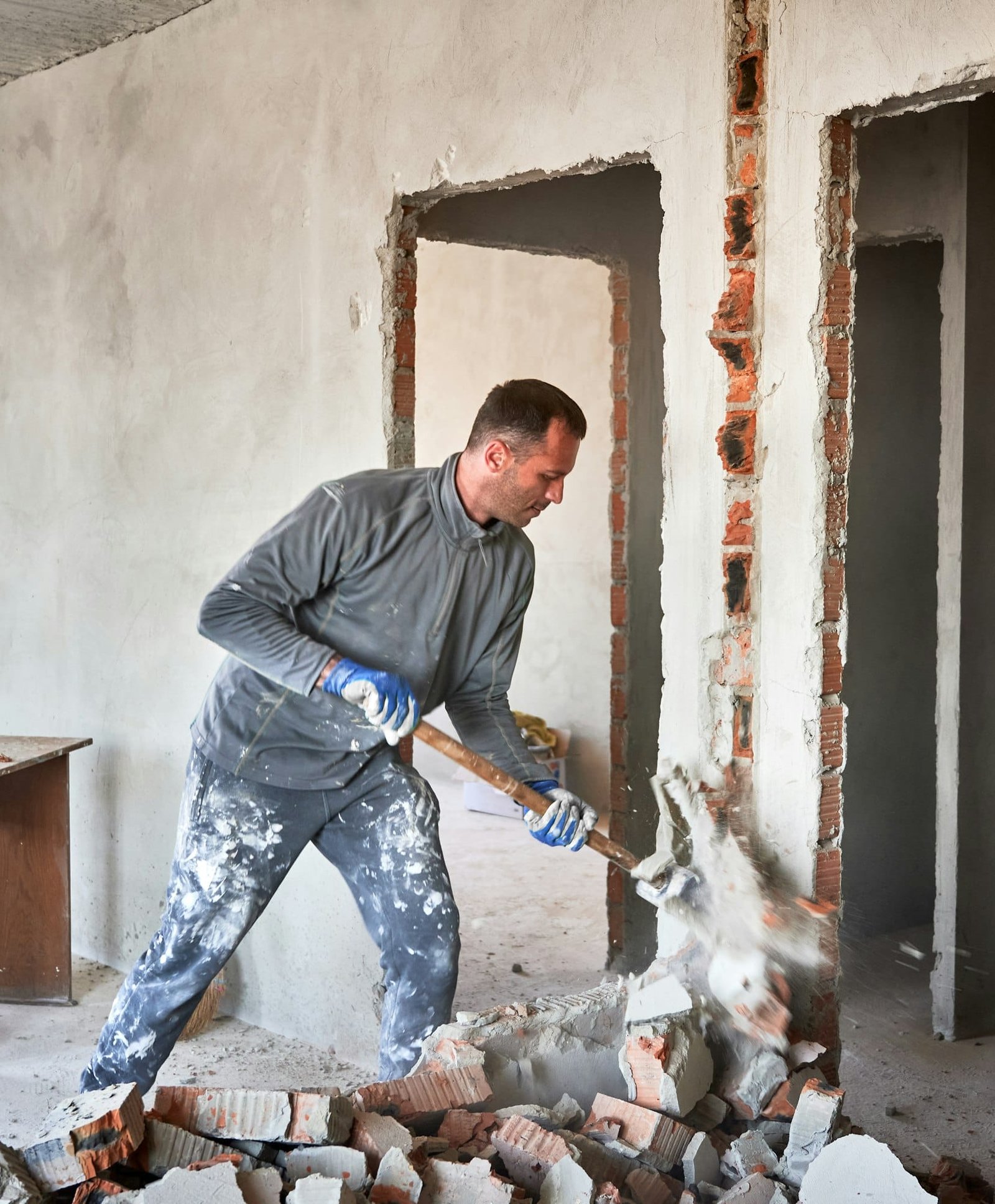 Male worker breaking wall with sledgehammer in apartment.
